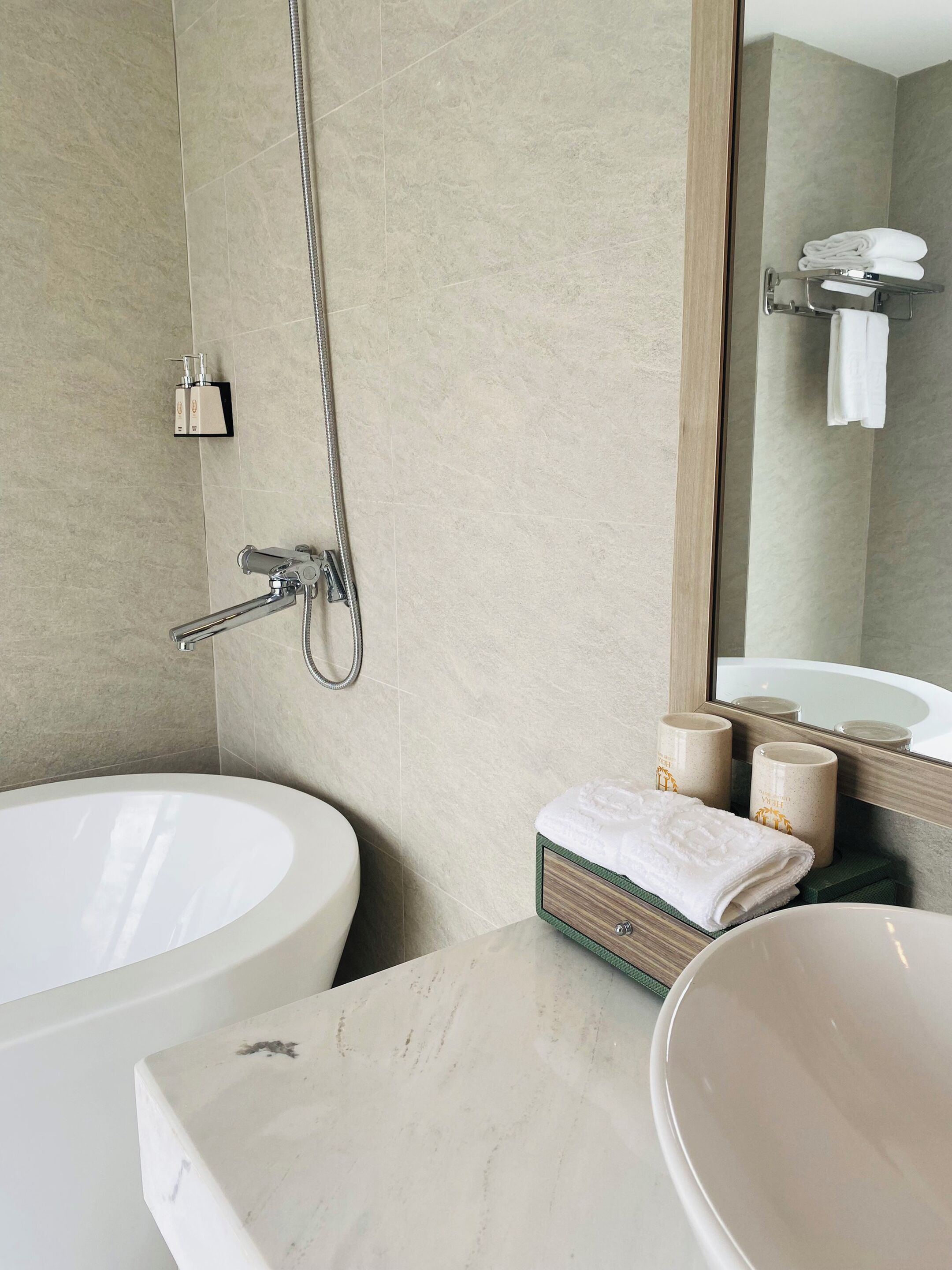 A bathroom with a large bathtub, a smaller sink, and a mirror. There are towels and toiletries on the counter.