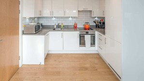 A modern kitchen with white cabinets, a microwave, a kettle, and a sink.