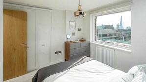 A bedroom with a bed, a dresser, a mirror, and a window with a city view.