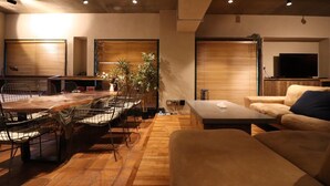 A modern living room with a wooden dining table, black wire chairs, a beige sofa, and a television on a wooden stand. - sunmalldai3 (Tokyo)