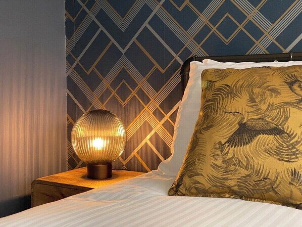 Un lit bien fait, avec un oreiller à motifs et une lampe décorative posée sur une table de chevet en bois.