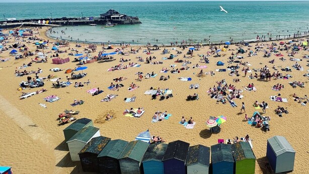Une plage avec de nombreux parasols et des gens qui prennent un bain de soleil. On aperçoit plusieurs petits abris de plage colorés au premier plan.