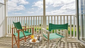 Un balcon avec deux chaises en bois et une table, une porte vitrée et une vue sur l’océan.