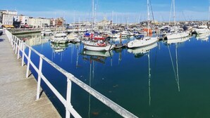 Un port de plaisance où sont amarrés de nombreux bateaux, un ciel bleu dégagé et une promenade en bord de mer.