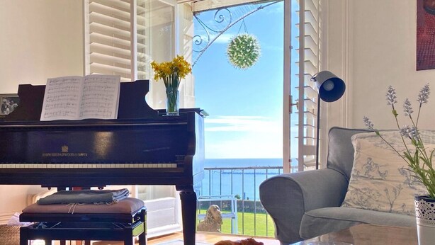 A piano with sheet music, a view of the sea, a balcony with a dog, and a painting of an American flag. - Recently refurbished and sleeping up to 4 guests, this stylish apartment offers stunning sea views, modern interiors, a fully equipped kitchen and a prime central location. Just moments from Ramsgate's Royal Harbour, beach, cafés and restaurants. (Kent)
