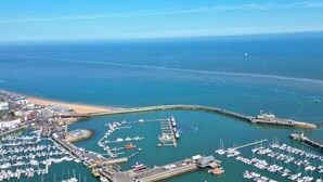 An aerial view of a coastal marina with boats docked, a pier, and a beach. - Recently refurbished and sleeping up to 4 guests, this stylish apartment offers stunning sea views, modern interiors, a fully equipped kitchen and a prime central location. Just moments from Ramsgate's Royal Harbour, beach, cafés and restaurants. (Kent)