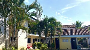 A swimming pool with a curved edge, surrounded by palm trees and a building with a tiled roof. - Tropical Beach Second Floor Studio with Hill view (Playas Del Coco)