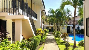 A pathway leading to a swimming pool surrounded by greenery and a building with balconies. - Tropical Beach Second Floor Studio with Hill view (Playas Del Coco)