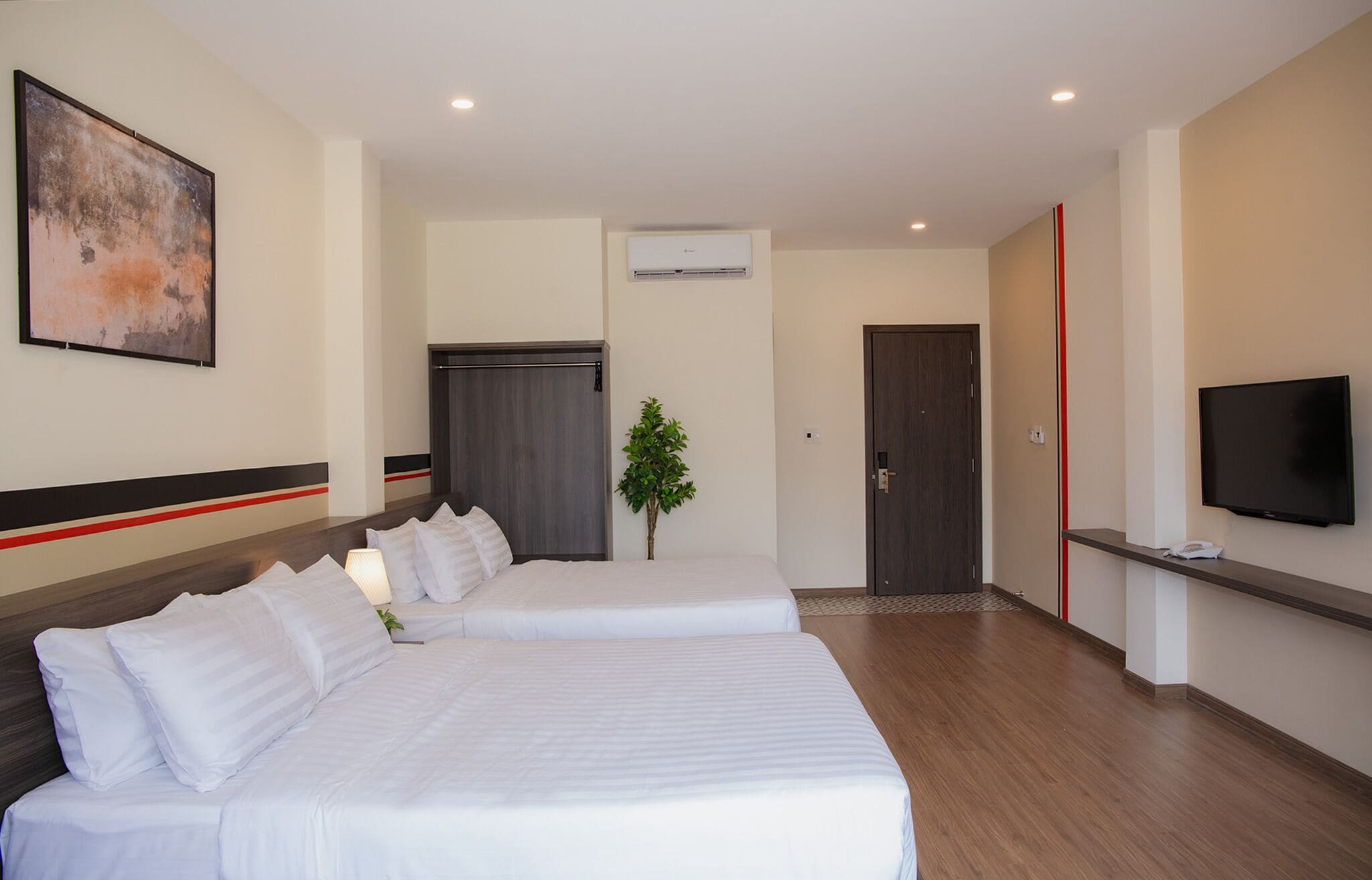 A hotel room with two beds, a TV, an air conditioning unit, a door, and a plant.