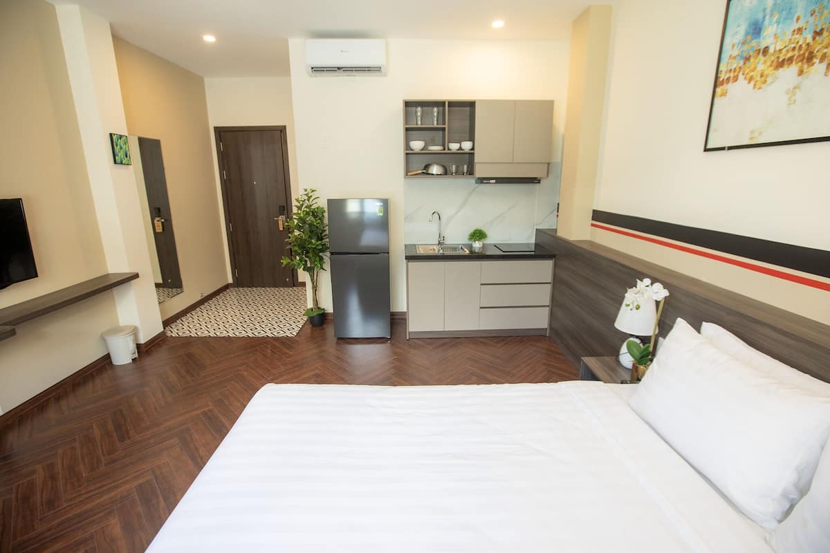 A hotel room with a bed, a kitchenette, a TV, and a potted plant.
