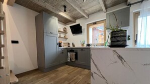 A modern kitchen with grey cabinets, a marble countertop, and a wooden ceiling.