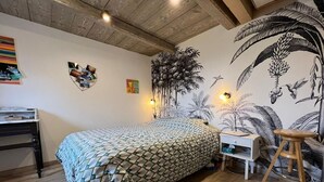 A bedroom with a bed, a desk, a chair, and a wall mural.