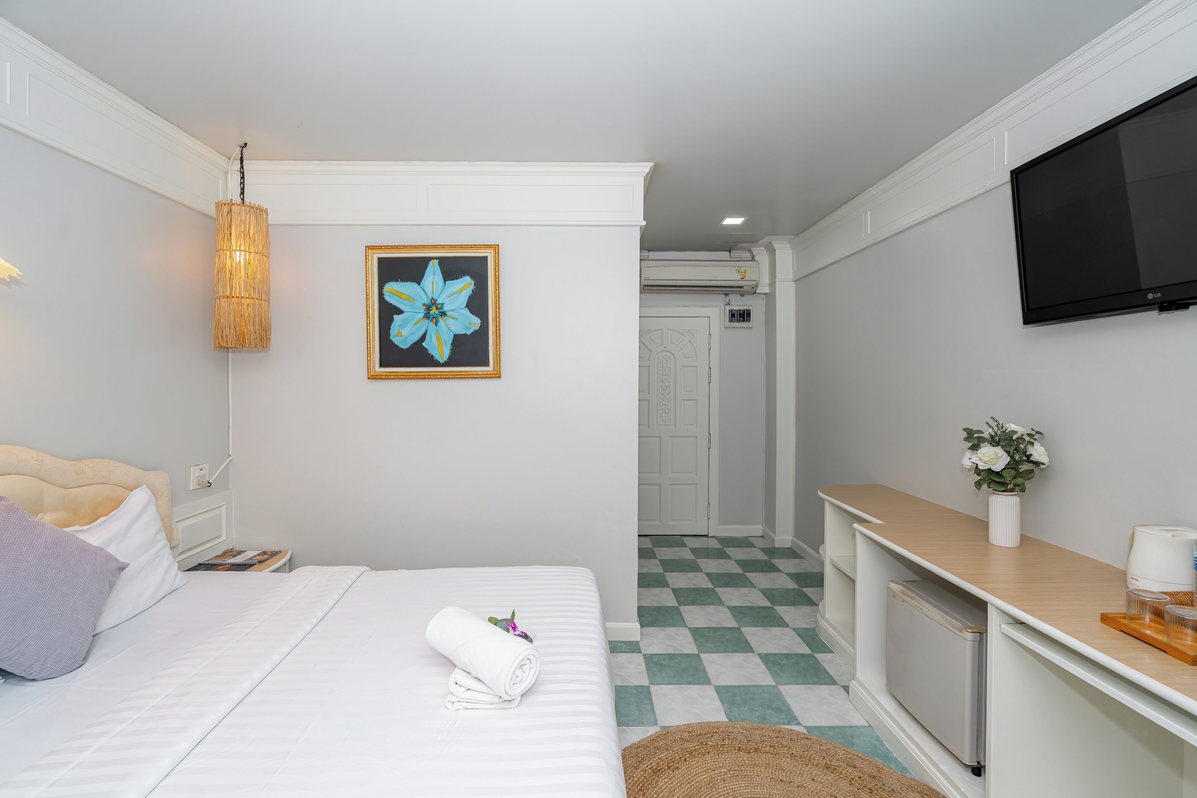 A hotel room with a bed, a television, a painting, and a checkered floor.
