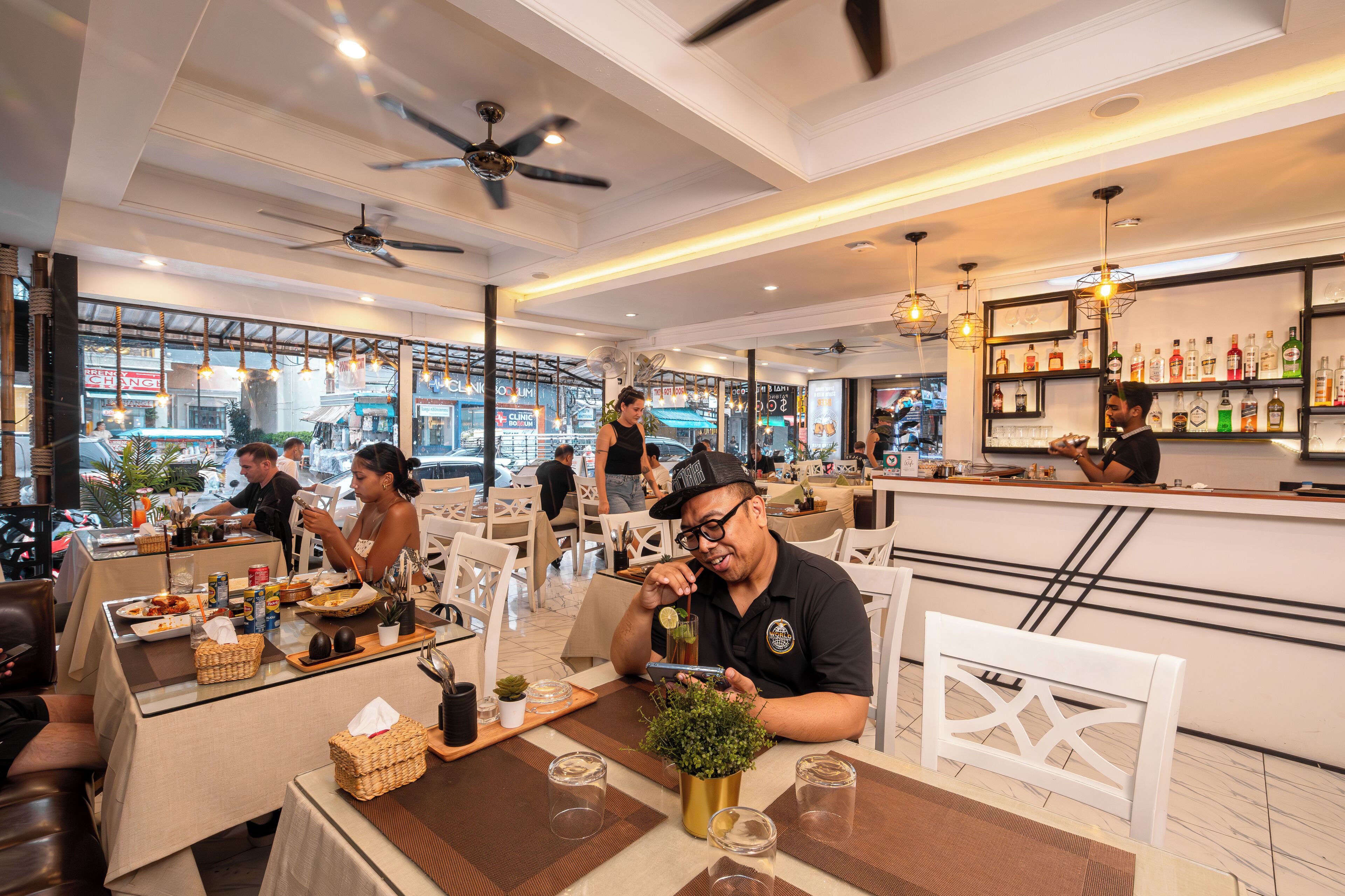 A restaurant with indoor seating, ceiling fans, and a bar area with shelves of bottles.