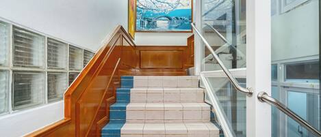 Una scala con ringhiere in legno e gradini rivestiti di tappeto blu che conduce a un pianerottolo con ringhiera in vetro.