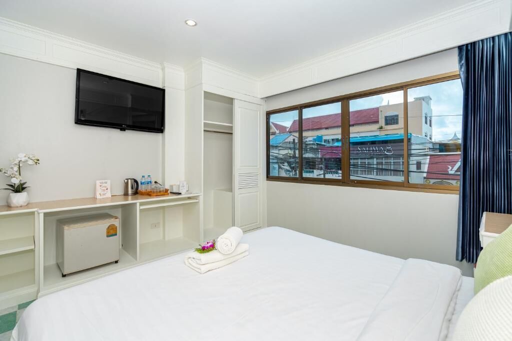 Habitación de hotel con cama, televisor montado en la pared, escritorio con computadora y ventana con vista a edificios.