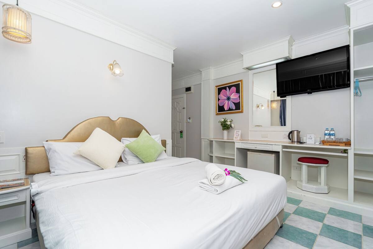 A hotel room with a bed, bedside table, desk, chair, and a large mirror.