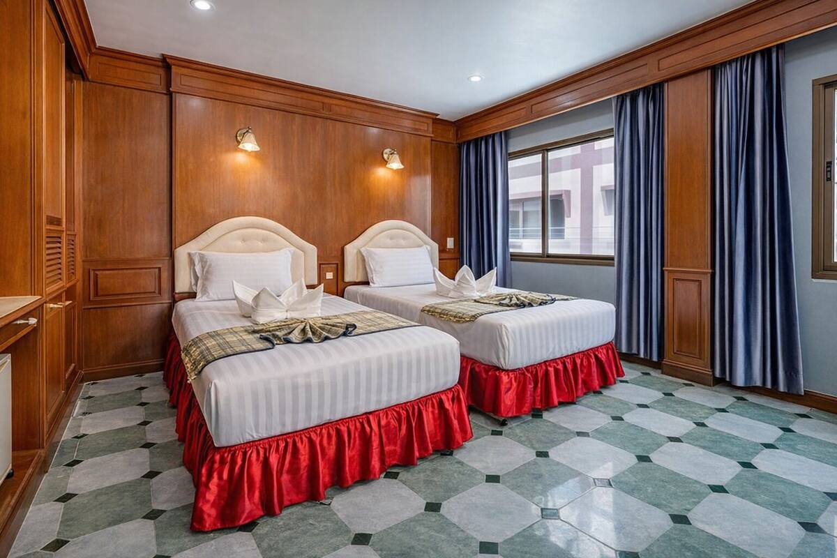 A hotel room with two beds, a checkered floor, wooden paneling, and a window with curtains.