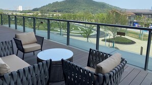A balcony with outdoor furniture, a view of a landscaped area, and a distant hill.