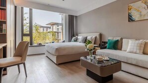 A modern hotel room with a bed, a sofa, a coffee table, and a bookshelf.