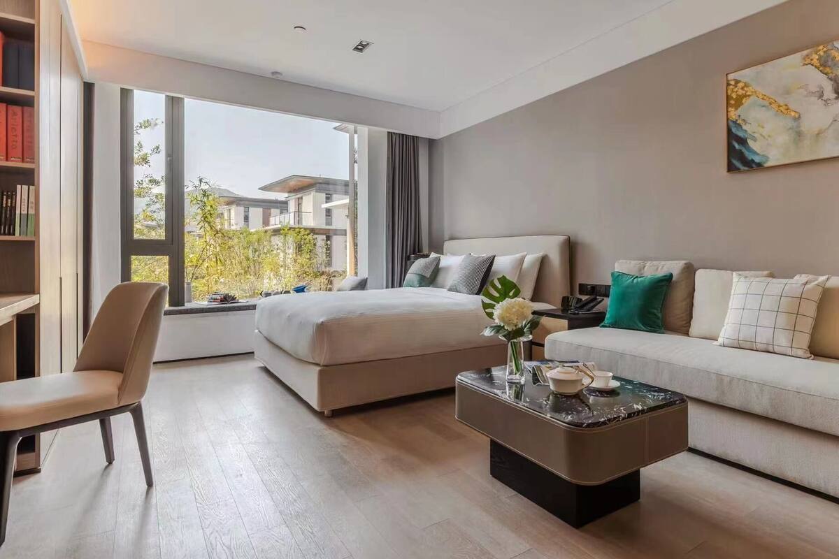 Una habitación de hotel moderna con una cama, un sofá, una mesita de centro y una estantería.