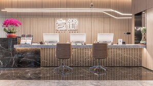 A modern reception desk with a wooden panel design, two chairs, and a potted plant.