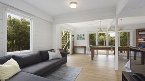 Un vaste espace de vie comprenant un canapé gris, une table de billard et un escalier menant à un balcon.