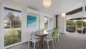 Un espace repas avec une table et des chaises en bois, de grandes fenêtres et des œuvres d’art accrochées aux murs.