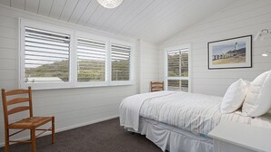 Une chambre à coucher avec un lit, deux chaises et de grandes fenêtres équipées de volets.