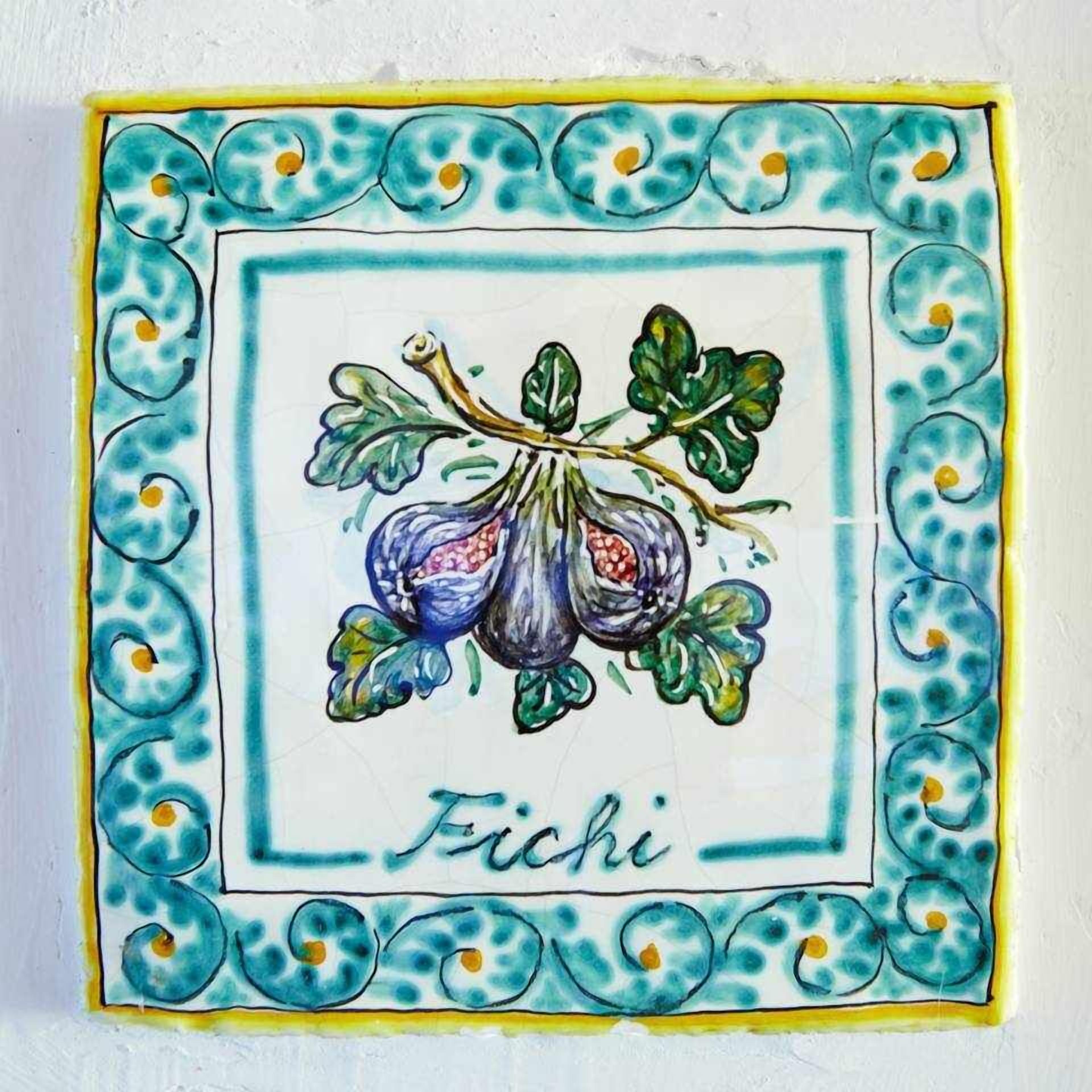 Une tuile ornée d’une bordure décorative et d’une illustration centrale représentant des figues, portant l’inscription « Fichi ».