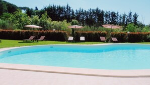 A swimming pool with lounge chairs and umbrellas, surrounded by greenery and trees. - Fichi Appartment (Firenze)