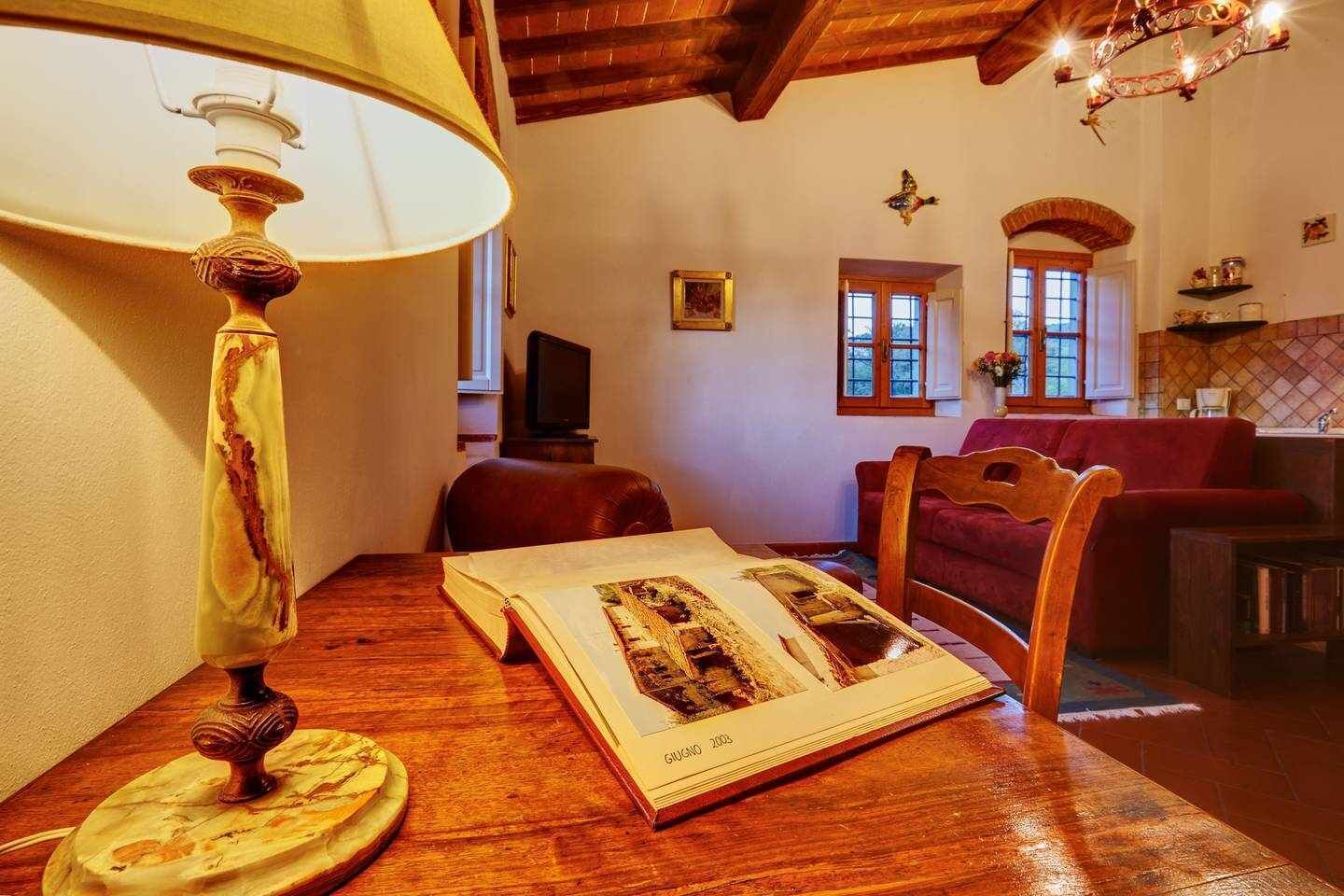 A cozy room with a wooden table, a lamp, a book, and a red sofa.