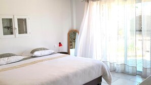 Un dormitorio con una cama grande, una mesita de noche, un espejo y una ventana con cortinas traslúcidas.