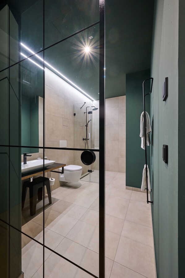 A modern bathroom with a glass partition, a sink, a toilet, and a shower area. - Hotel der Einrichter (Straubing)