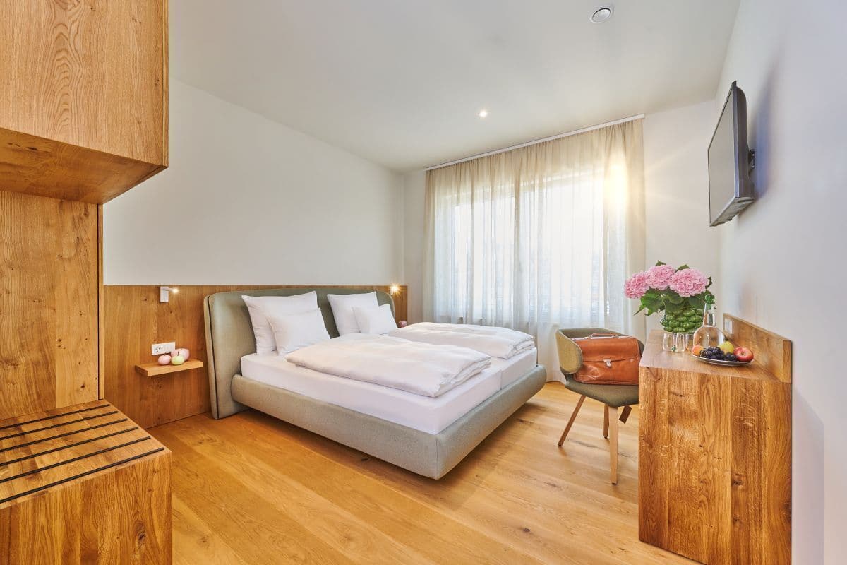 A modern hotel room with a large bed, a wooden desk, a chair, and a TV mounted on the wall.