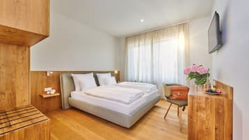 A modern hotel room with a large bed, a wooden desk, a chair, and a TV mounted on the wall.