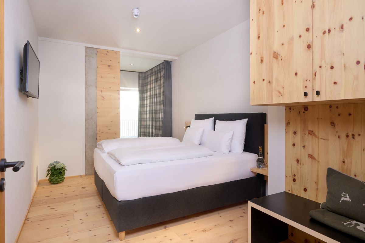 Un dormitorio moderno con una cama grande, paneles de madera en las paredes, un televisor montado y una planta pequeña.