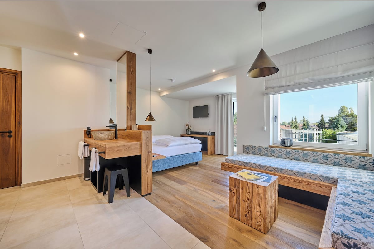 A modern bedroom with a wooden desk, a bed, and a seating area by a large window.