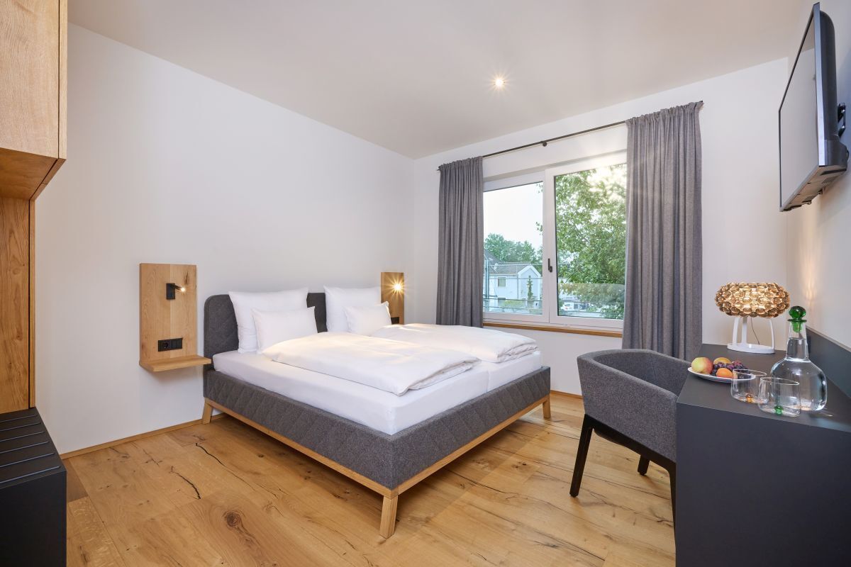 Una habitación de hotel moderna con cama, escritorio, silla, televisor y ventana con cortinas.