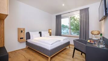 Una habitación de hotel moderna con cama, escritorio, silla, televisor y ventana con cortinas.