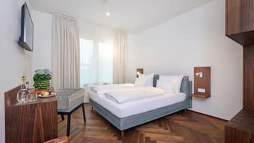 Ein modernes Hotelzimmer mit einem großen Bett, einem Schreibtisch, einem Sessel und einem kleinen Tisch mit Pflanze und Obst.
