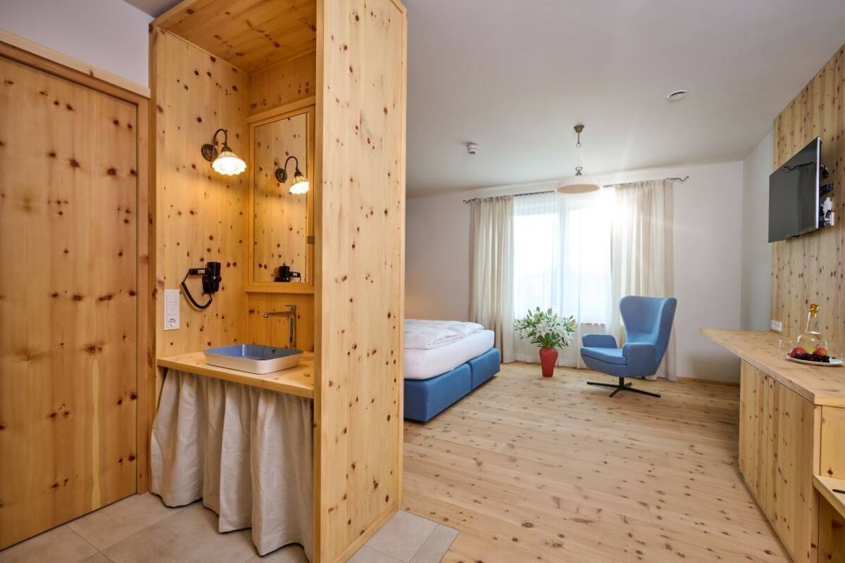 A room with a wooden floor, a bed, a chair, a TV, and a small table with fruit.