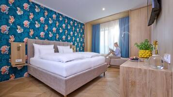 Una habitación de hotel con cama, escritorio, televisión y ventana con cortinas.