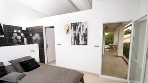 Une chambre à coucher moderne avec un lit, une salle de bain aux carreaux noirs et blancs, et un balcon aménagé avec du mobilier d’extérieur.