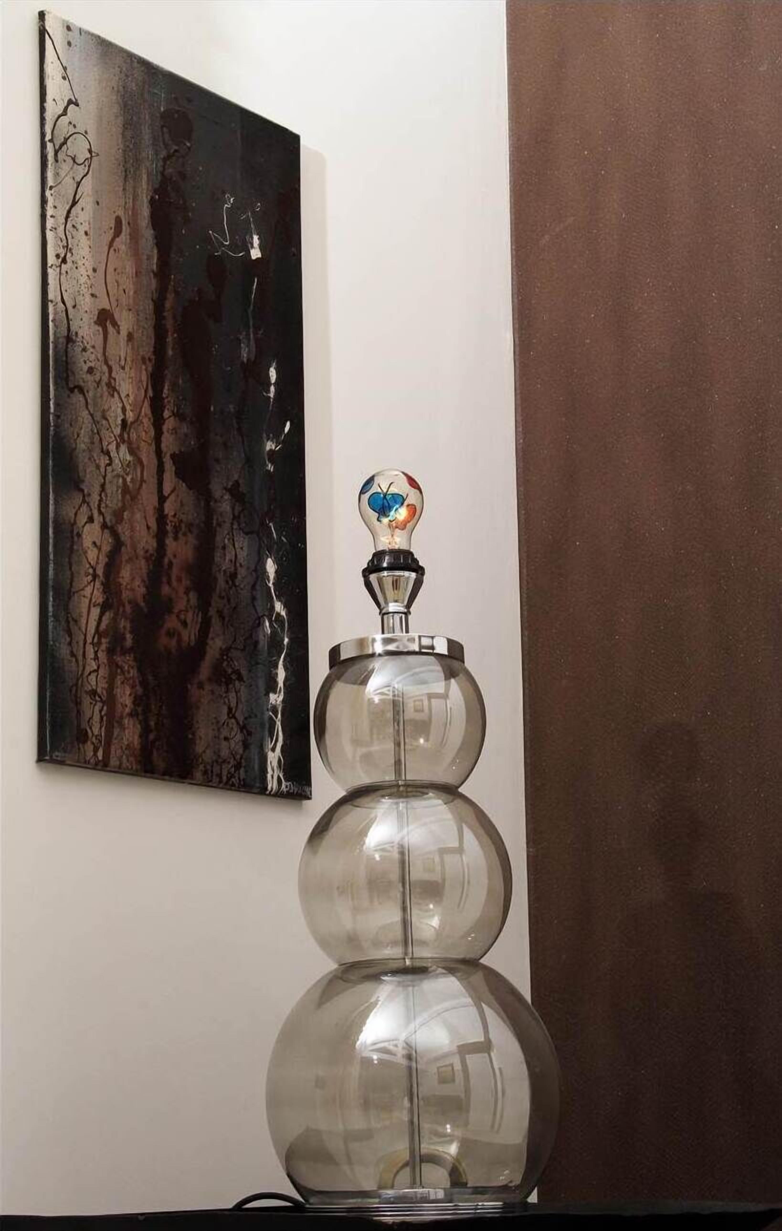 A glass sculpture with a metallic base and a decorative top, placed on a table against a wall with a painting.