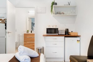 A compact hotel room with a kitchenette, a bed with a white towel, a small wooden table, and a white refrigerator. - Private Studio on Fryer (Queenstown)