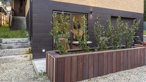 A modern building with a dark facade, a wooden deck, and a garden area with plants. - Private Studio on Fryer (Queenstown)