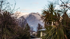 A mountain with a clear sky, surrounded by trees and a building with a sloped roof. - Private Studio on Fryer (Queenstown)