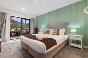 A bedroom with a large bed, a nightstand, a chair, and a view through a sliding door. - Private Studio on Fryer (Queenstown)