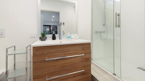A modern bathroom with a glass shower enclosure, a wooden vanity with a mirror, and a small potted plant. - Private Studio on Fryer (Queenstown)